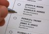 Hand holding pen near presidential election ballot.