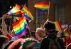 Bear Pascoe at a pride parade holding a rainbow flag among a cheering crowd