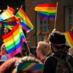 School Makes BOLD ‘LGBTQ+’ October Declaration Bear Pascoe at a pride parade holding a rainbow flag among a cheering crowd