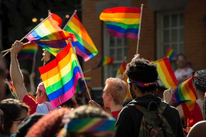 shutterstock_1099936808 Bear Pascoe at a pride parade holding a rainbow flag among a cheering crowd
