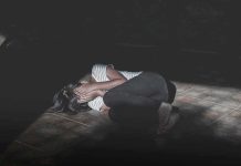 Person curled up on a tiled floor covering their face