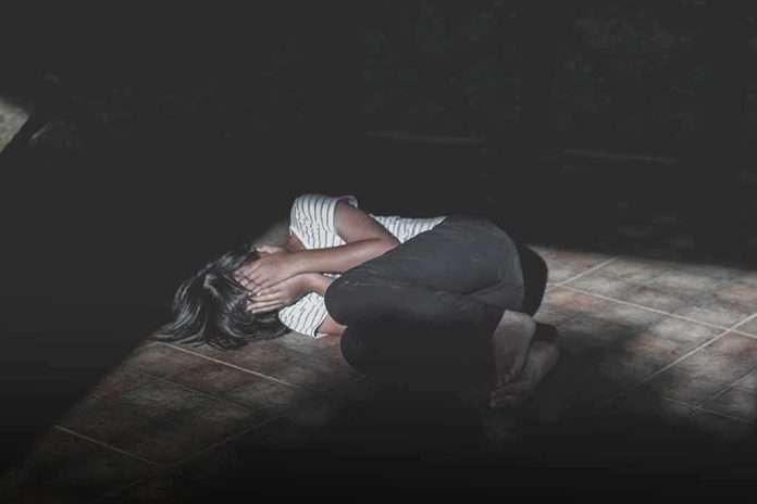 shutterstock_1103911892 Person curled up on a tiled floor covering their face