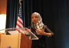 Omar’s Allies Call Her Raid Political PAYBACK Ilhan Omar speaking at a podium with a microphone