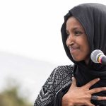 Ilhan Omar FUMING Over Detained US Candidate Ilhan Omar speaking at a microphone with hand on chest