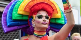 Pastor Found GUILTY Over Drag Story Hour Protest Drag performer in vibrant rainbow costume raising an arm at a parade
