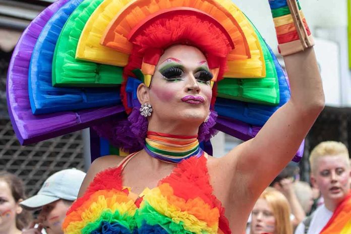 shutterstock_1451344577 Drag performer in vibrant rainbow costume raising an arm at a parade