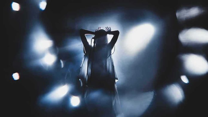 shutterstock_1505017997 Silhouetted singer on stage amid dramatic blue spotlights