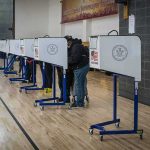 Washington State Fights DOJ Over NONCITIZEN Ballots Voters at polling booths in a gymnasium