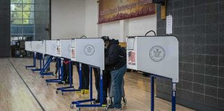 Washington State Fights DOJ Over NONCITIZEN Ballots Voters at polling booths in a gymnasium
