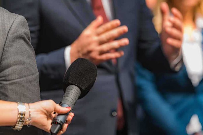 shutterstock_2168392357 Reporter holding microphone toward speaker in suit