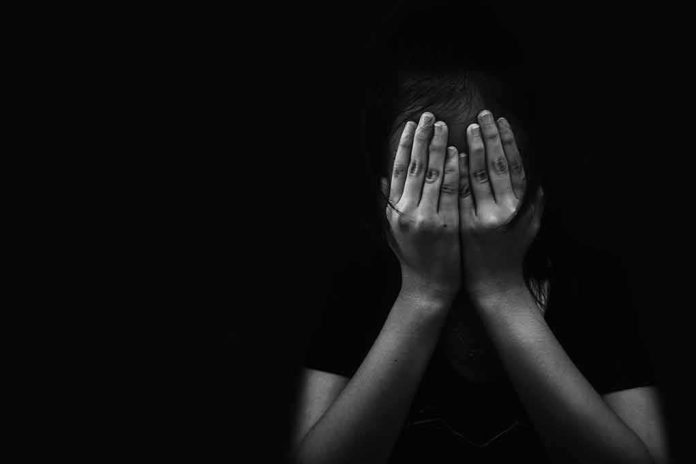 shutterstock_692287723 person covering face with both hands in darkness