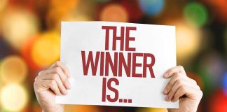 Hands holding a sign reading "The Winner Is..."