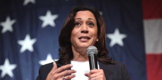 Woman speaking with microphone, American flag background.