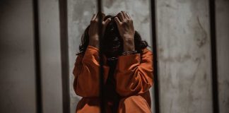 Person sitting in jail cell wearing orange jumpsuit