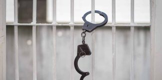 Handcuffs hanging on white metal bars.