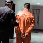 Officer escorting handcuffed prisoner in orange jumpsuit