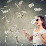 Woman happily holding phone with money flying around