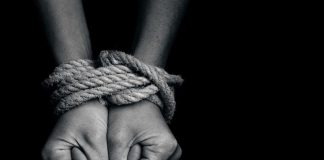 Hands tied with rope against black background