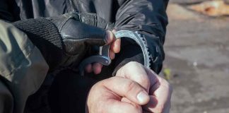 Gloved officer handcuffing a person's hands outdoors