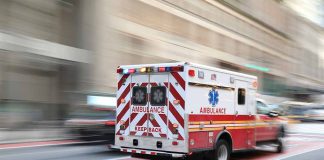 Red and white ambulance driving in the city.