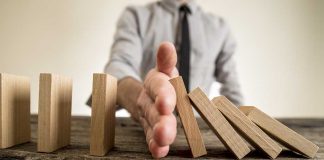 Hand stops falling dominoes on wooden table