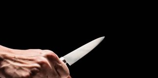 Hand holding a knife against a black background
