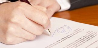 Person signing a document with a pen