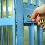 Hand unlocking blue prison cell with keys