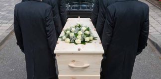 Four people carrying a coffin with white flowers