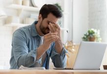 Man rubbing eyes holding glasses near laptop