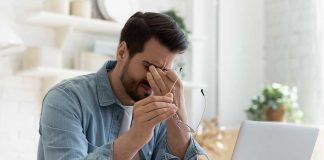 Man rubbing eyes holding glasses near laptop