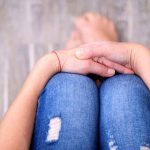 Person sitting with folded hands on knees.