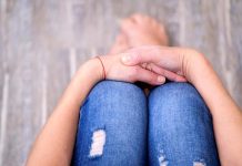 Person sitting with folded hands on knees.