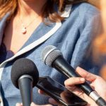 Woman in blue jacket speaking to microphones