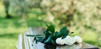 White roses on a polished wooden casket outdoors