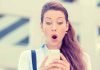 Surprised woman looking at her smartphone outdoors