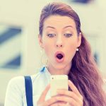 Surprised woman looking at her smartphone outdoors