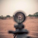 Rifle scope aimed at a distant target outdoors.