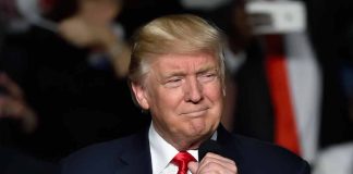 Trump holding microphone wearing suit and red tie