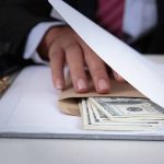 Hand concealing cash under a folder on a desk