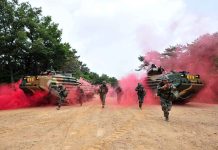 Soldiers running from armored vehicles with red smoke