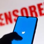Phone displaying Twitter app with CENSORED in background