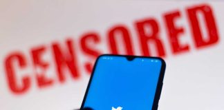 Phone displaying Twitter app with CENSORED in background