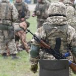 Soldiers in camouflage gear gathered on grass field