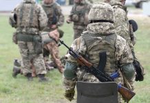 Soldiers in camouflage gear gathered on grass field