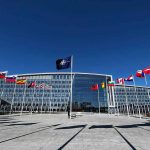 Flags outside NATO headquarters building under clear blue sky
