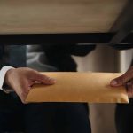 Two people exchanging envelope under table
