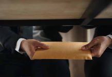 Two people exchanging envelope under table