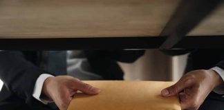 Two people exchanging envelope under table