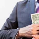 Person in suit putting dollars in jacket pocket